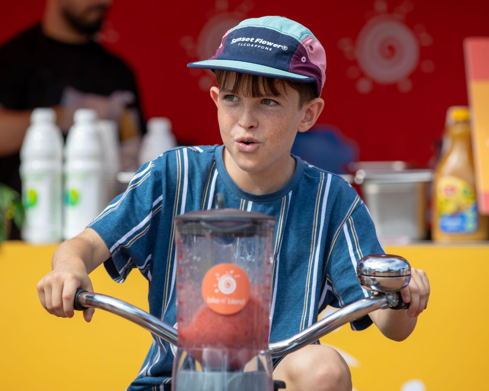 Boy riding a smoothie bike, with colourful marquee and serving station in the background