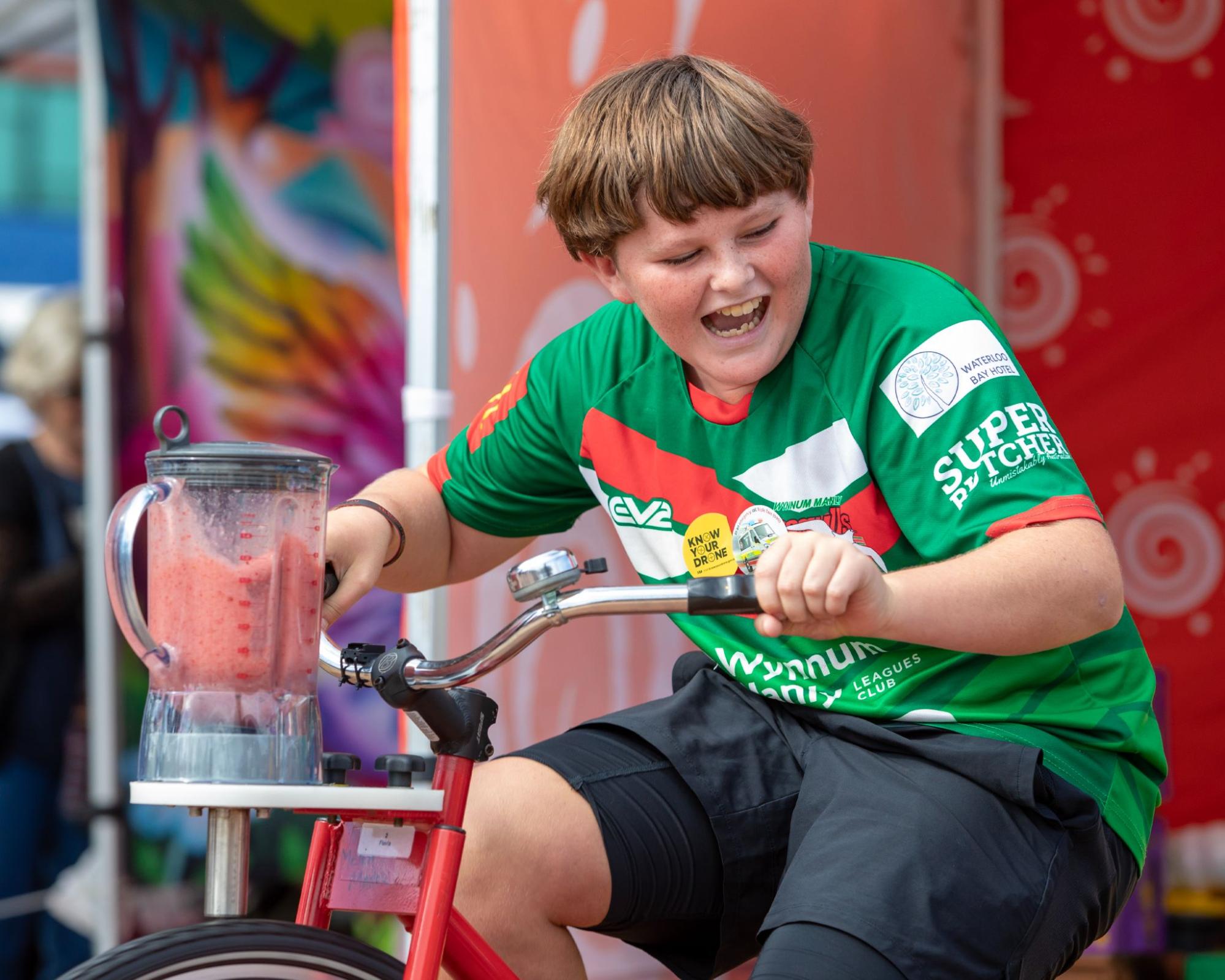 A boy laughing as he rides a blender bike with a red fruit smoothie on top